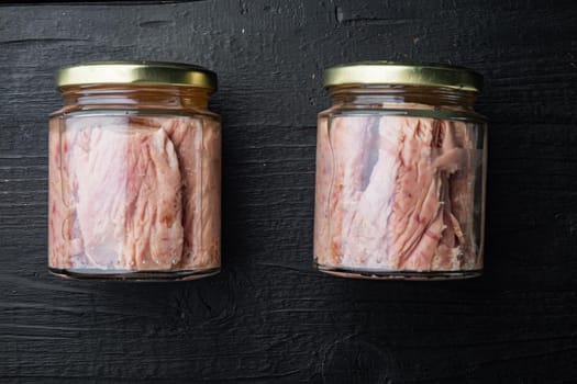 Tuna fillet meat in glass jar, on black wooden background, flat lay