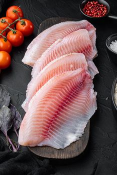 Raw white fish tilapia, with basmati rice and cherry tomatoes ingredients, on black background, top view