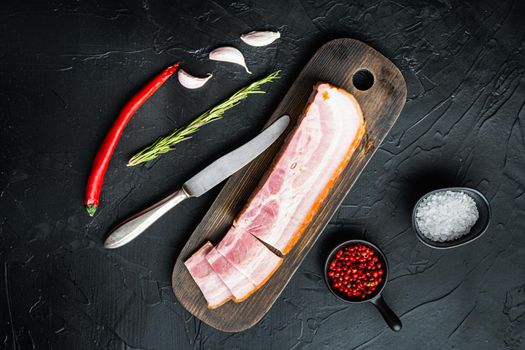 Bacon pancetta cut and sliced with herbs on black background, top view.