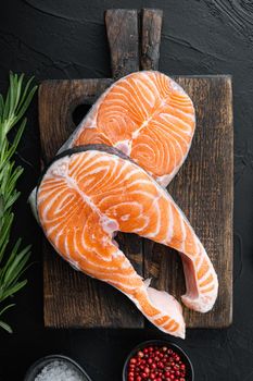 Trout steak raw fish with herbs, over black background, top view.