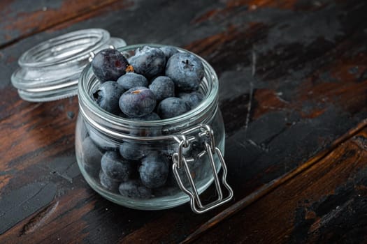 Ripe blueberry in glass jar with space for text on old wooden background.