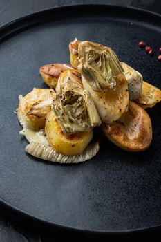 Baked potato, artichoke with fennel al forno, on black textured background