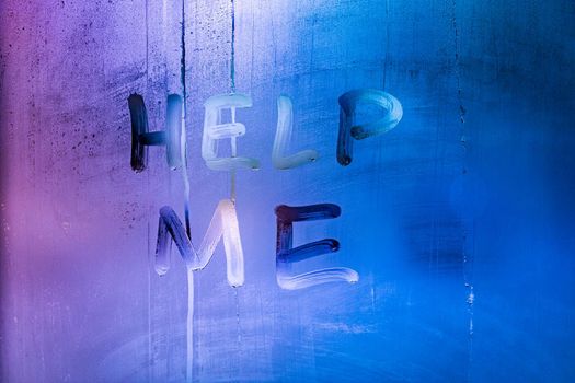 the words help me handwritten on night wet window glass with purple and blue color gradient in blurry background