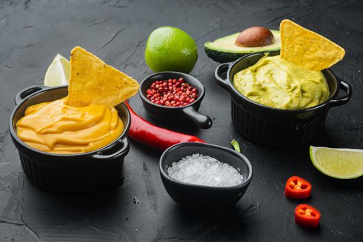 Green guacamole and yellow cheese dip sauce for traditional, Mexican tacos, on black background