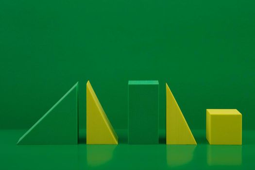 Abstract composition with green and yellow geometric figures triangles, rectangular and cube on green glossy table against green background. Concept of background template for advertising