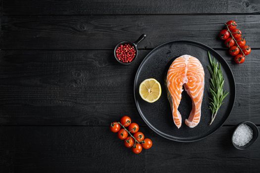 Slice of red fish salmon with herbs, on black wooden surface, flat view with copy space.