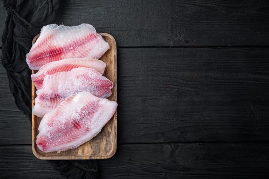 Frozen, white fish fillet, on black wooden background, top view with copy space for text