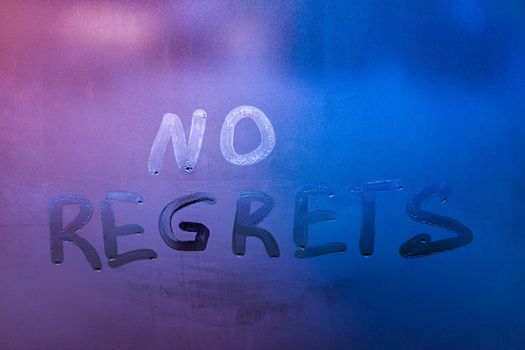 words no regrets hand written on purple-blue night foggy window glass - closeup with selective focus abstract concept