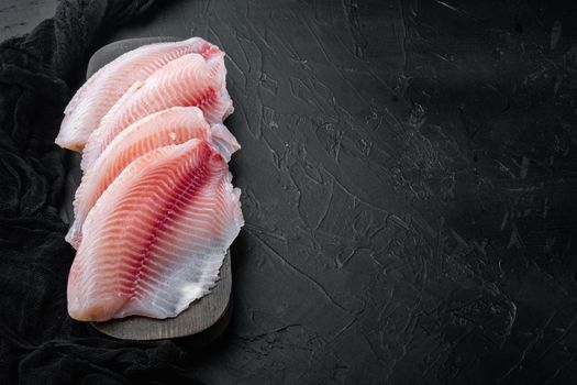 Tilapia fish, skinless meat, on black background with copy space for text