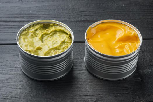 Canned cheese and guacamole sauce in can, on black wooden background