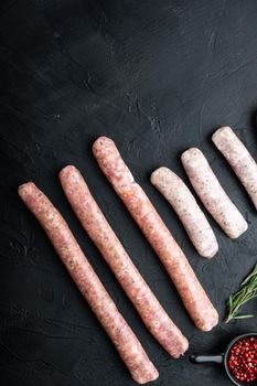 Fresh raw pork, beef and chicken sausages, top view, on black background.