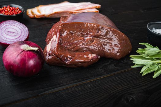 Beef liver with bacon and onion on black wooden background.