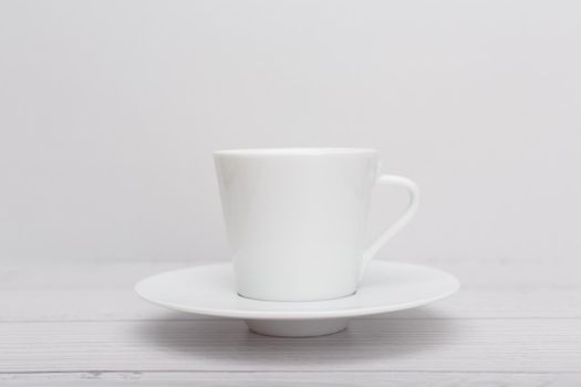 Selective focus, white ceramic tea or coffee cup with a saucer on white wooden table against white blurry background. High quality photo