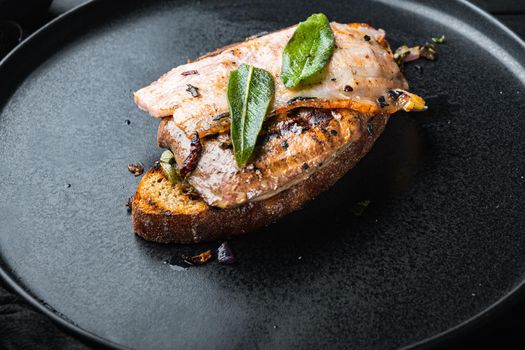 Liver bacon and onions on bread cooked meal on plate on black surface.