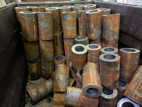 rusted thick steel pipe chunks after sawing in industrial crate waiting for machining operations in factory storage