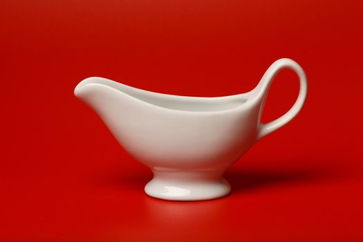 Minimalistic still life with white ceramic gravy boat on bright red background. High quality photo