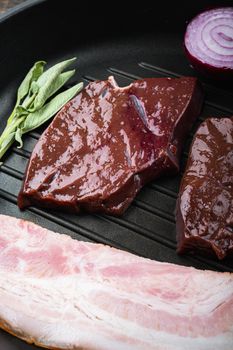 Raw beef liver sliced with bacon on grill pan over rustic background.