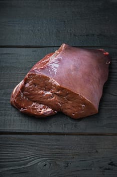 Raw liver on black wooden background with copy space.