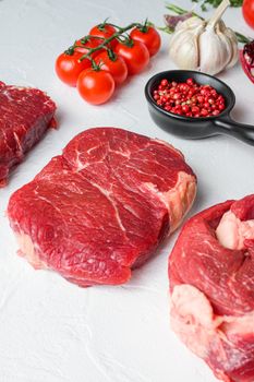 Beef cuts Chuck eye roll, top blade, rump steak with red wine in glass and bottle, herbs and pomegranate. Organic meat. White textured background. Side view vertical