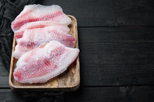 Frozen, white fish fillet, on black wooden background with copy space for text