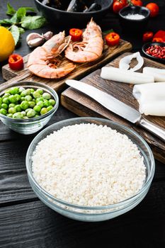 Raw paella ingredients over black wooden table, food photo.