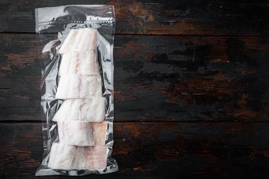 Raw haddock fish skinless plastic vacuum packaged, on old wooden table, top view with copy space for text