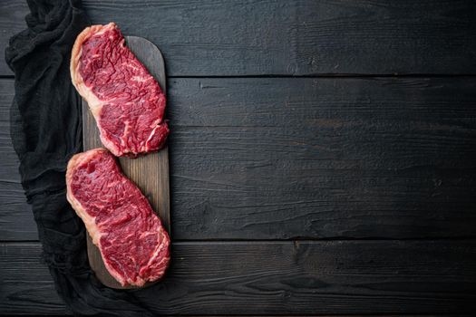 Strip loin steak, raw marbled beef meat, on black wooden table, top view, with copy space for text