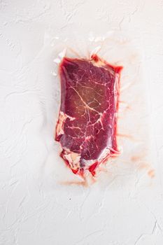Raw rump beef steak, vacuum packed organic meat for sous vide cooking on white concrete textured background, top view