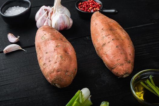 Sweet potato or batat with ingredients, on black wooden background.