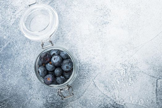 Ripe blueberry in glass jar, flat lay with space for text, on textured background.