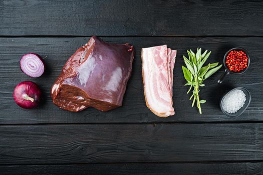 Raw liver with bacon and onion on black wooden background, flat lay.