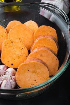 Cajun sweet potatoes for baking with herbs and spices on black background.