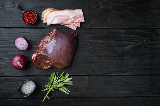 Raw liver with bacon and onion on black wooden background, flat lay with copy space.
