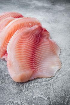 Raw tilapia fish fillet meat cuts, on gray background