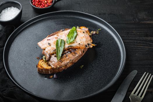 Liver bacon and onions on bread cooked meal on plate on black surface.