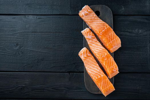 Fresh raw salmon fillet cuts, on black wooden table, flat lay with space for text
