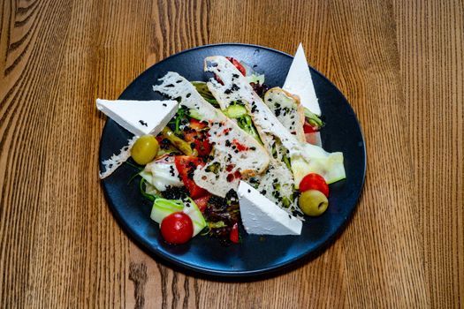 Salad on a plate. Salad with cheese, bread, ofochas and fruits on a black plate.