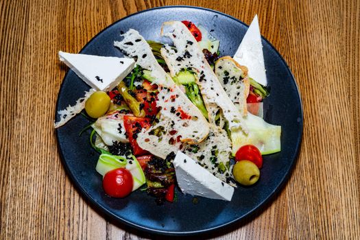 Salad on a plate. Salad with cheese, bread, ofochas and fruits on a black plate.