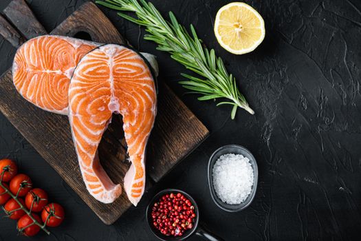 Salmon steak raw fish with herbs, over black background, top view.