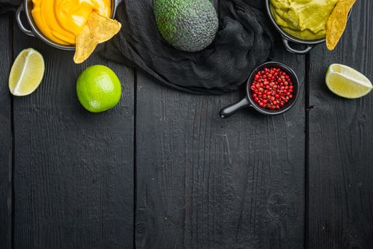 Green guacamole and yellow cheese dip sauce for traditional, Mexican tacos, on black wooden background, top view or flat lay with copy space for text