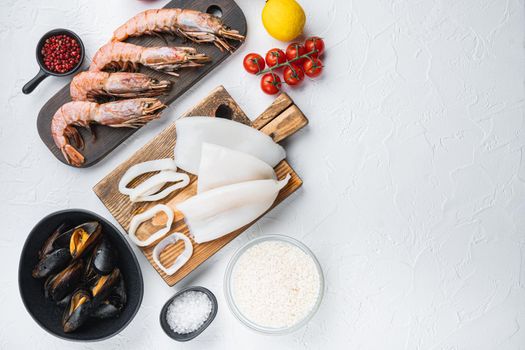 Fresh seafood assortment for paella on white textured background, flat lay with copy space, food photo.