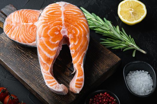 Raw salmon steak with herbs, over black background.