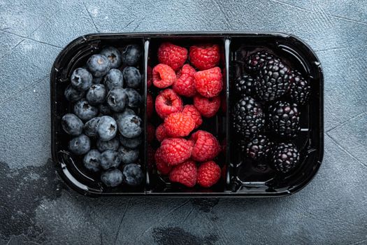 Ripe berries in tray from market, blueberries, raspberry with blackberry, top view, on grey background
