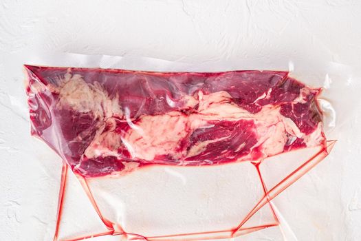 Vacuum packed organic chuck roll steak on white concrete textured background,top view