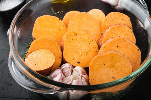 Cajun sweet potatoes for baking with herbs and spices on black background.