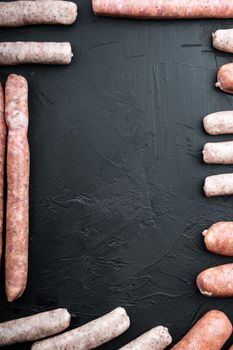 Fresh raw pork, beef and chicken sausages, frame or border concept, top view with space for text, on black background.