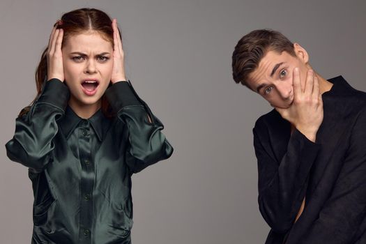 A woman in a dress covered her ears with her hands and a puzzled man in a suit holds his hand near his face. High quality photo