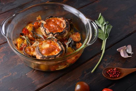 Portobello mushrooms,baked with cheddar cheese, cherry tomatoes and sage in glass pot on old wooden background side view