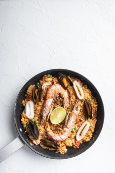 Seafood and chicken paella with rice, mussles, shrimps,chicken, tomatoes and wine in pan on white textured background, flat lay with copy space, food photo.