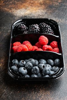 Fresh berries packed in tray, blueberries, raspberry and blackberry, on old dark table